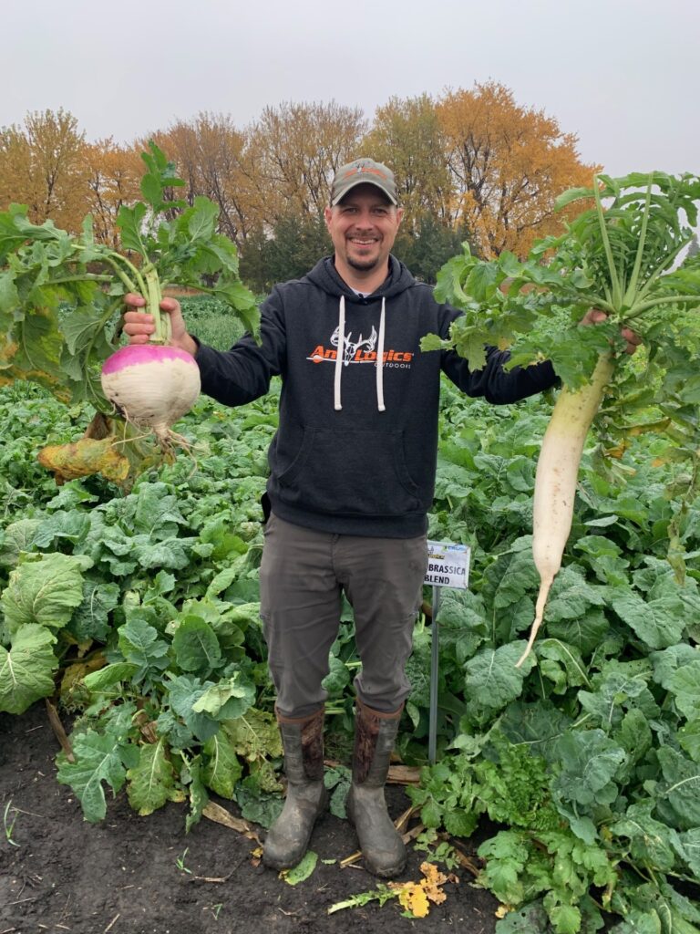 Tim Neuman holding up the results of planting the Pro Brassica blend - a huge purple top turnip and radish